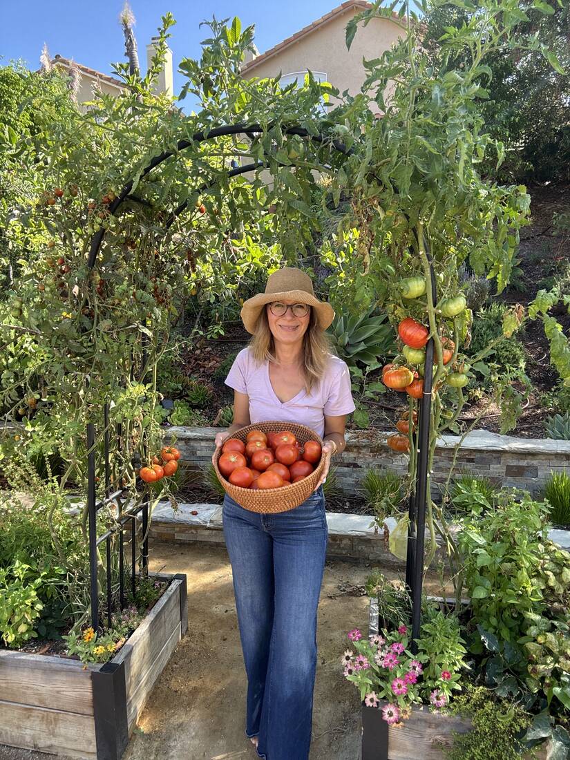 Marynika smiling under an arch trellis, holding a basket of freshly harvested tomatoes